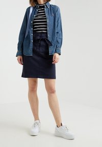 Denim košile na knoflíky přes černobíle pruhovaný top, spárovaná s námořnickou sukní a bílými platformovými teniskami. Sukně má detail vázané mašle.