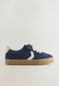Marineblaue Sneaker mit einem Klettverschlussriemen und weißen Schnürsenkeln, mit einem beigen Akzent nahe der Ferse, vor einem schlichten Hintergrund.