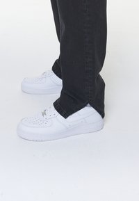 Vita sneakers med perforerade tår och en texturerad sula, tillsammans med svarta jeans i rak passform med sidslitsar vid fållen.