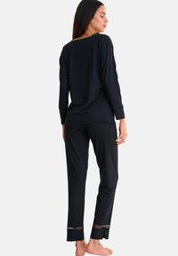 Ensemble de salon noir comprenant des manches longues, des accents de dentelle sur les côtés, et un pantalon droit avec une finition en dentelle à l'ourlet. Tissu doux et respirant.