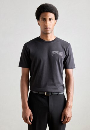 Zwarte t-shirt met korte mouwen en een logo op de linkerkant van de borst, gecombineerd met zwarte broeken en een riem met een rechthoekige gesp. Gladde textuur.