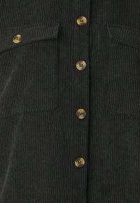 Dark green corduroy shirt featuring vertical ribbing, six large buttons with a mix of colors, and two front pockets.