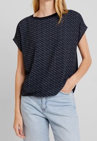 Marinblå kortärmad topp med en diskret all-over-mönster, som har en avslappnad passform och rund halsringning, tillverkad av ett lätt och mjukt material.