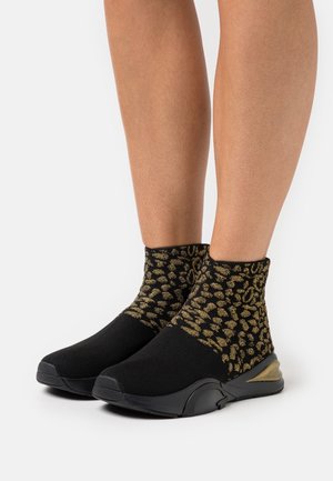 Chaussettes noires tricotées avec un motif léopard doré, présentant un design élégant et texturé ainsi qu'une semelle en caoutchouc noir pour l'adhérence et le soutien.