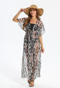 Kimono translucide noir et blanc à motifs abstraits, ouvert sur le devant, ceinturé à la taille, avec des manches courtes, associé à un haut noir et un chapeau à large bord.