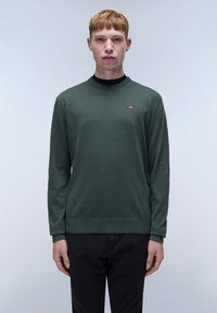 Groene lange mouwen trui in een zachte breimateriaal, met een ronde hals en een klein logo accent op de borst. Gecombineerd met donkere broeken.