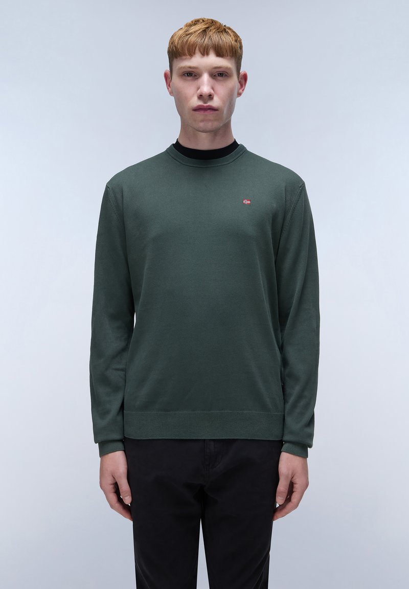 Groene lange mouwen trui in een zachte breimateriaal, met een ronde hals en een klein logo accent op de borst. Gecombineerd met donkere broeken.