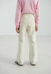 Pantalon large couleur crème, duveteux, avec une taille élastique et une texture douce, associé à un haut à manches longues rose clair.