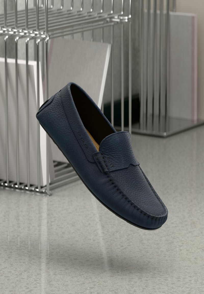 Mocasines de cuero azul marino con un acabado texturizado, que presentan una costura elevada y una punta redondeada. Diseño ligero, situado sobre un fondo minimalista.