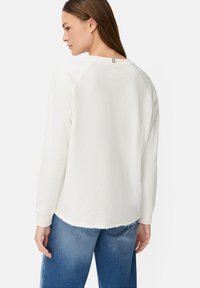 Witte sweatshirt met lange mouwen, een ontspannen pasvorm, raglanmouwen en een gebogen zoom. De stof heeft een gestructureerde afwerking. Gecombineerd met denim jeans.