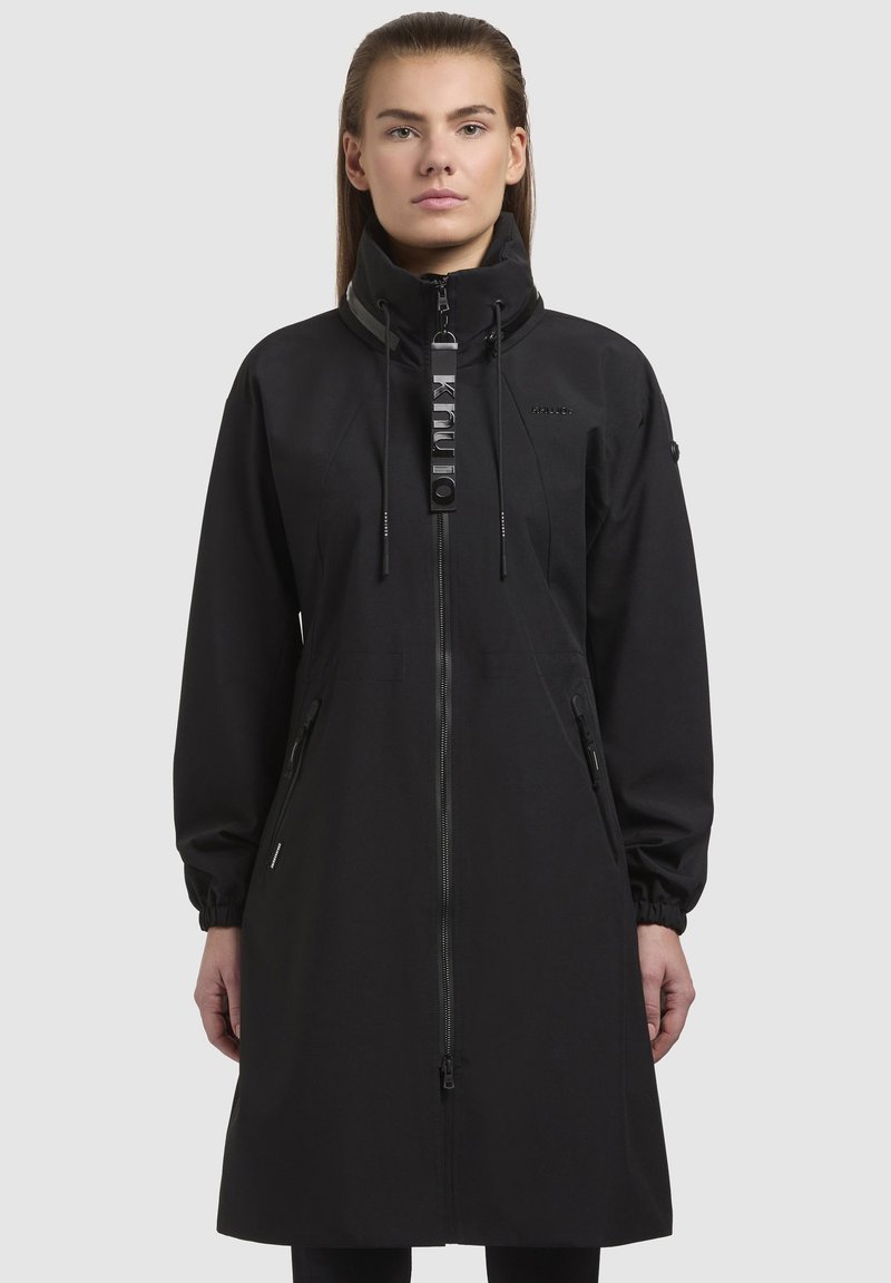 Cappotto lungo nero con colletto alto, chiusura con zip e coulisse. Presenta tasche laterali con zip e polsi elasticizzati. Tessuto dalla texture liscia.