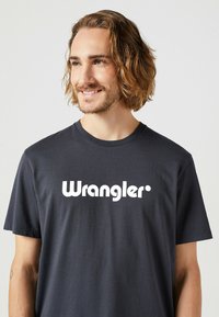 Svart bomulls t-shirt med en vit "Wrangler" logotyp i fet stil, rund halsringning, korta ärmar och mjuk textur.