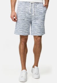 Pantalones cortos azul con un estampado, fabricados en un tejido texturizado, con una cintura elástica ajustable, bolsillos laterales y un diseño geométrico. Combinados con zapatillas blancas.