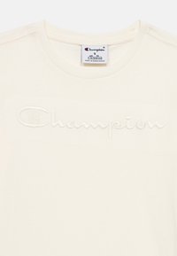 Κρεμ T-shirt Champion με κεντημένο λογότυπο στο στήθος και ετικέτα μεγέθους 7/8 (126/131 εκ.) στο εσωτερικό της λαιμόκοψης.