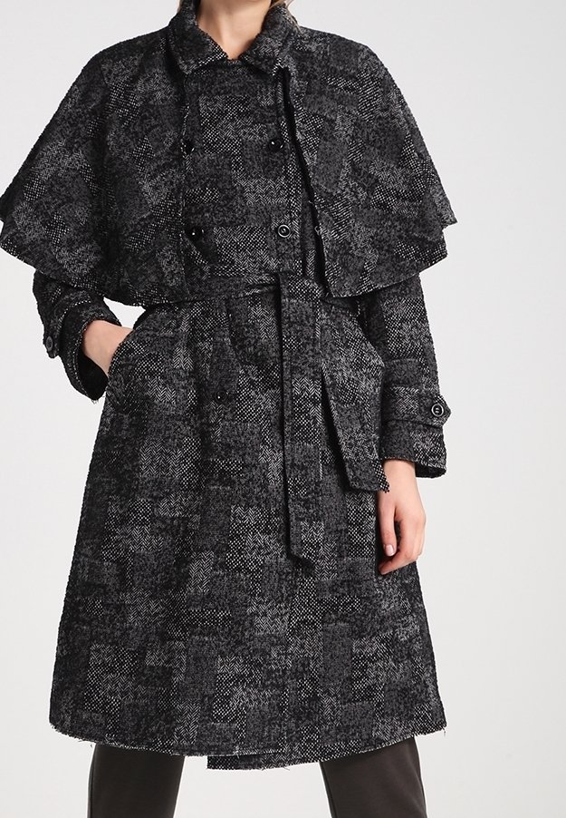 Černobílý vzorovaný vlněný kabát s návrhem pláště, páskem v pase a knoflíkovými detaily. Dlouhé rukávy s knoflíkovými detaily na manžetách.