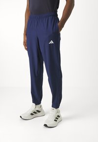 Dunkelblaue Sporthose mit einem elastischen Bund, schmal zulaufenden Beinen und seitlichen Taschen. Auf dem linken Oberschenkel befindet sich ein kleines weißes Adidas-Logo.