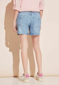 Bermudas de mezclilla de color azul claro con los dobladillos doblados, bolsillos traseros y una cintura ajustada, combinadas con zapatillas blancas con detalles en rosa.