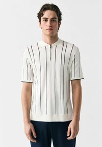 White knitted polo shirt with navy vertical stripes, short sleeves, and a half zip closure at the collar. Smooth texture and fitted design.