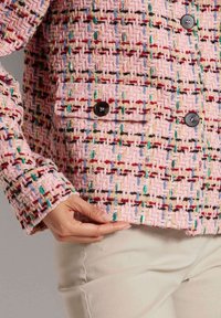 Gelaagde roze blazer met een geweven patroon met veelkleurige draadjes, twee zwarte knopen en een relaxte pasvorm. Close-up van de randdetails.