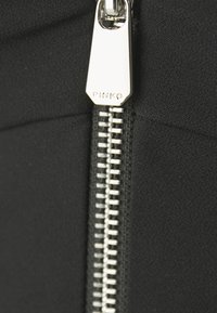 Nærbilde av svart stoff med en sølvglidelås og et merke med teksten "PINKO", som viser en glatt tekstur og skinnende detaljer.