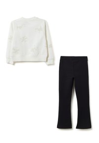 Sweat-shirt blanc à manches longues avec des motifs subtils de chiens de dessin animé, associé à un pantalon droit noir uni, posé à plat sur un fond blanc.