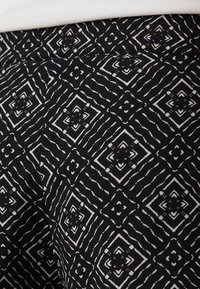 Černá tkanina se geometrickým bílým vzorem s diamantovými tvary a vlnitými čarami, vytvářející texturovaný design na povrchu.