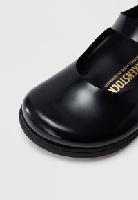 Μαύρο παπούτσι με στρογγυλεμένη μύτη, λείο δερμάτινο επάνω μέρος με γυαλιστερή υφή και ματ ελαστική σόλα. Διαθέτει σχέδιο με κοψίματα κατά μήκος τ ου ανοίγματος.