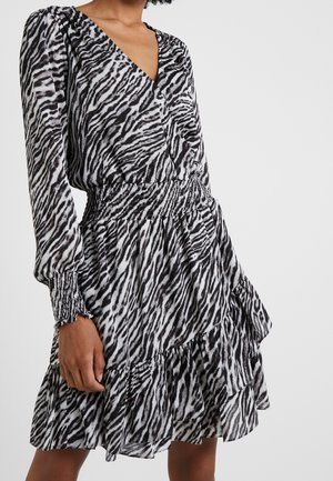 Vestido de manga larga con estampado de cebra en blanco y negro, escote en V, cintura y puños fruncidos, y falda con volantes de varios niveles, llevado por una persona.