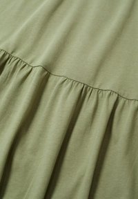 Olivi vihreä mekko, jossa on kerätty frillireuna. Se on valmistettu pehmeästä, kevyestä kankaasta, jolla on sileä pinta ja yksinkertainen muotoilu.