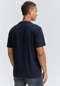 Tricou bleu marin cu mânecă scurtă, cu croială lejeră, guler rotund și textură netedă, prezentat din spate. Material din amestec de bumbac.
