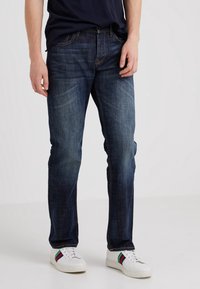 Tmavě modré džíny s rovnými nohavicemi, designem pěti kapes a jemným vyblednutím, doplněné bílými teniskami se multibarevnými pruhy.