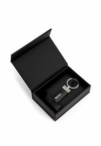 Black keychain in a black box, featuring a chrome circular attachment and a textured leather strap with "BOSS" branding.