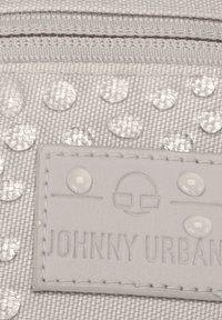 Portefeuille en tissu gris clair avec des points transparents en relief et une étiquette en cuir texturé avec le texte en relief "JOHNNY URBAN". Détail de zip visible.