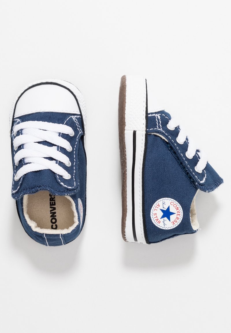 Paire de petites chaussures bébé Converse bleu marine avec lacets blancs, embouts en caoutchouc et écusson logo sur le côté, vues de dessus et de côté.