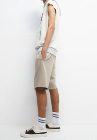 Light gray sleeveless hoodie with a plush texture, paired with beige knee-length shorts with frayed edges. White sneakers with black accents.