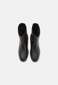 Bottines en cuir noir avec une texture lisse, bout rond et panneaux latéraux élastiques. Design minimaliste sans matériel visible ni motifs.