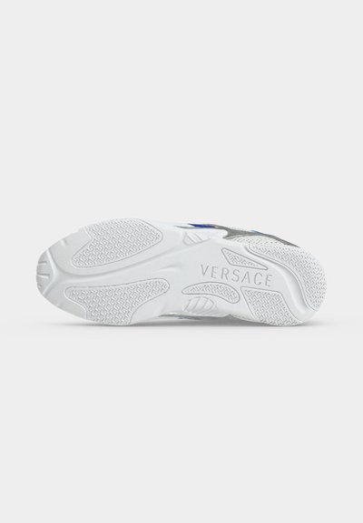 Semelle blanche de sneaker avec des grips texturés et le mot Versace embossé au centre de la semelle sur un fond uni.