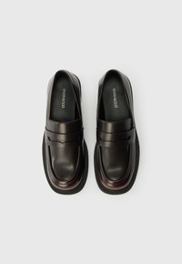Scarpe mocassino in pelle marrone scuro con suola esterna nera spessa e dettagli decorativi a fascia sulla parte superiore.