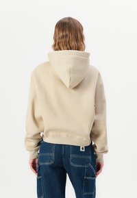 Hoodie corto beige con un grande cappuccio e polsini a coste, abbinato a jeans cargo blu scuro con molte tasche.