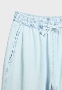 Pantalon de jogging en denim bleu clair avec taille élastique et cordon de serrage, doté de poches latérales et de détails de couture visibles.