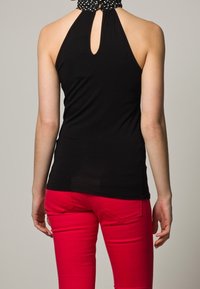 Haut halter noir avec un détail de dos en trou de serrure, associé à un jeans rouge ajusté, mettant en valeur un tissu lisse et un contraste de couleurs audacieux.