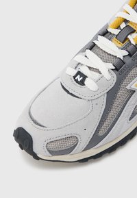 Hall hallisest seemishallist ja võrgust jooksujalats valgete paelte, kollaste detailide ja musta kummist tallaga. Märkimisväärne logo ja hingav disain.