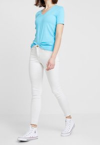 Valkoinen puuvillainen V-pääntie T-paita, joka on yhdistetty slim-fit valkoisiin farkkuihin ja valkoisiin kanvaakengiin. Paidassa on lyhyet hihat ja rento istuvuus.