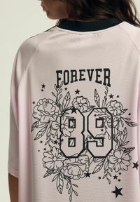 Różowa siatkowa koszulka z czarnym kołnierzykiem. Zawiera napis "FOREVER" nad numerem "89", otoczony grafikami kwiatowymi i gwiazdkowymi.