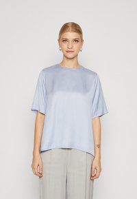 Lyseblå satin topp med korte ermer og rund hals. Har en løs passform og en jevn, myk tekstur.