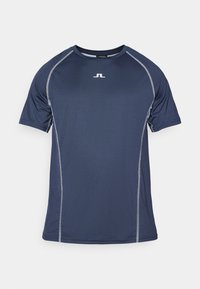 Tumši zils sporta T-krekls ar īsām piedurknēm, kontrastējošām pelēkām šuvēm un mazu logo uz krūtīm. Izgatavots no mitruma novadošiem materiāliem.
