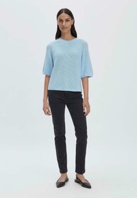 Vaaleansininen neulottu lyhythihainen neule, jossa on tekstuuri, yhdistetty mustiin kapeisiin farkkuihin ja mustiin liukupohjaisiin kenkiin.