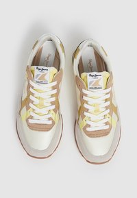 Zapatos deportivos con un exterior de cuero blanco, amarillo y marrón claro, que cuentan con cordones blancos, un cuello acolchado y una suela de goma texturizada.