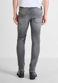 Jeans slim fit de color gris desvaído con dos bolsillos traseros. El detalle de costura y un ligero desgaste realzan la apariencia texturizada del denim.