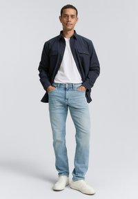 Marine blauwe overhemdbloes, witte t-shirt, lichtblauwe jeans en witte sneakers. Casual fit met twee borstzakken en een klassiek ontwerp.